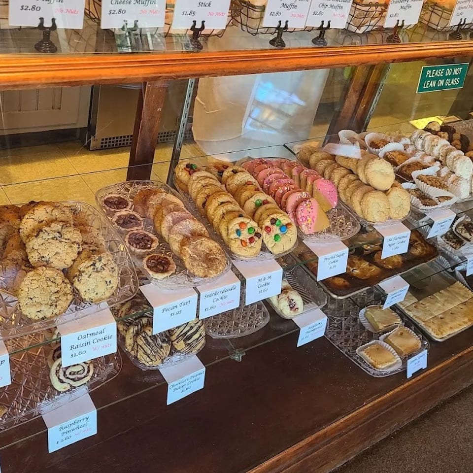 Glass bakery display case filled with labeled cookies, pastries, muffins, and decorated treats.