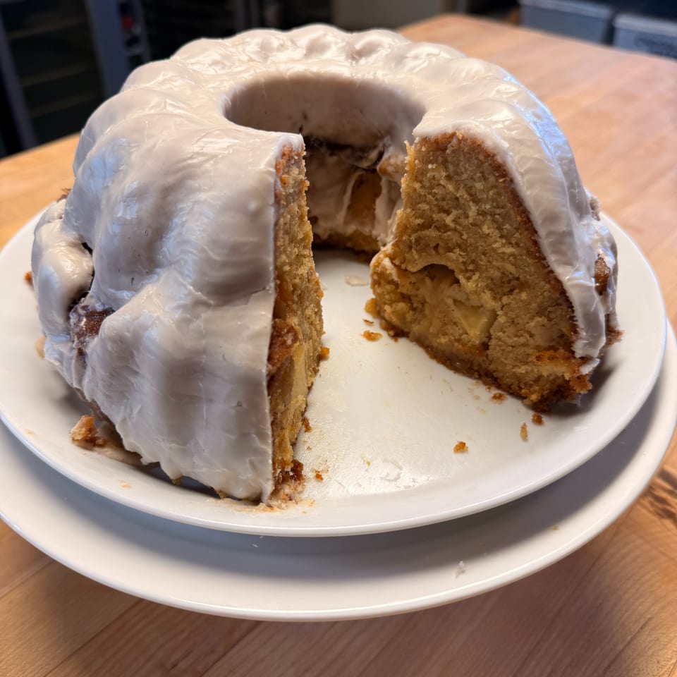 Glazed ring cake with a slice removed, revealing a moist golden crumb and filling on a white plate.